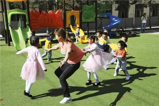青海乐都,幼教志愿者带着孩子们玩老鹰捉小鸡的游戏.jpg